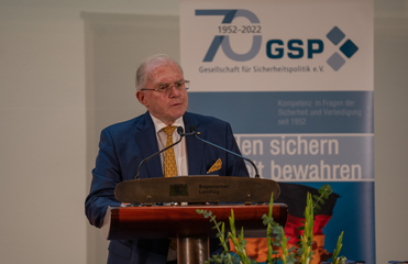 Mann im blauen Anzug spricht an einem Rednerpult vor einem GSP-Jubiläumsbanner (1952-2022), „Bayerischer Landtag“ sichtbar.