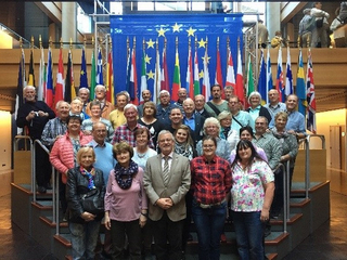 Eine große Gruppe von Menschen unterschiedlichen Alters steht auf Stufen vor einer Ausstellung von EU- und Mitgliedstaatenflaggen.