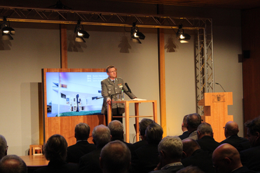 Ein Bundeswehr-Soldat in Uniform spricht an einem Rednerpult vor Publikum, mit Baden-Württemberg-Wappen.