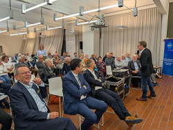 Ein Mann hält einen Vortrag vor einem aufmerksamen Publikum von Erwachsenen und Senioren bei einer DWT-Veranstaltung.