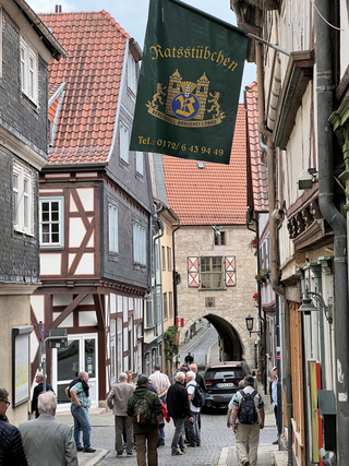 Altstadtgasse mit Fachwerkhäusern, Menschen, einem Bogen und dem Banner 'Ratsstübchen' einer Brauerei.
