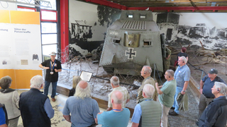 Eine Tourgruppe besichtigt im Museum einen historischen Panzer namens 'Wotan' mit Eisernem Kreuz. Ein Guide erklärt Details.