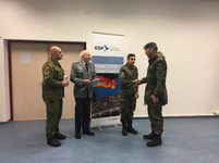 Vier Männer in Militäruniform, zwei schütteln Hände, vor einem GSP-Banner mit der Aufschrift 'Frieden sichern Freiheit bewahren'.