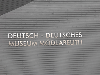 Schild des Deutsch-Deutschen Museums Mödlareuth an einer grauen Holzfassade, das an die ehemalige innerdeutsche Grenze erinnert.