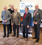 Fünf Männer, darunter ein Soldat in Uniform, stehen lächelnd vor einem Banner der Gesellschaft für Sicherheitspolitik.