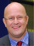 Lachendes Porträt von Jan Muehlfeit, einem glatzköpfigen Mann mit Brille, Anzug und roter Krawatte.