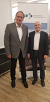 Zwei Männer in Sakkos und Brillen lächeln vor einem Banner der Gesellschaft für Sicherheitspolitik (GSP).