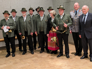Deutsche Jagdhorngruppe in Tracht, darunter eine Frau, posiert mit einem Militäroffizier und einem Mann im Anzug.