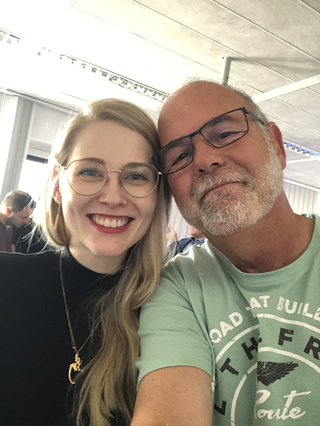 Eine lächelnde blonde Frau mit Brille und ein Mann mit grauem Bart und Brille machen ein Selfie.