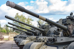 Reihe von Armeepanzern, die ihre großen Kanonenrohre und Türme vor einem blauen Himmel mit weißen Wolken zeigt.