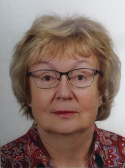 Porträt einer älteren Frau mit blonden Haaren, Brille und gemustertem Oberteil.
