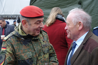 Ein deutscher Soldat im Flecktarn-Anzug und rotem Barett unterhält sich lächelnd mit einem älteren Herrn.