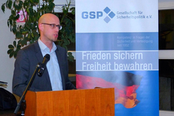 Glatzköpfiger Mann mit Brille spricht an einem Rednerpult mit Mikrofon vor einem GSP-Banner mit Deutschlandflagge.