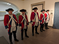 Fünf Männer in historischen roten Militäruniformen mit Dreispitzhüten stehen in einer Reihe.