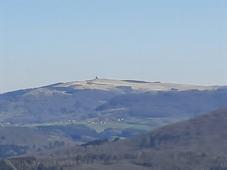 Ferner Berg mit Turm auf dem Gipfel, über sanften Hügeln und kleinen Dörfern unter klarem blauem Himmel.