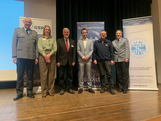Sechs Personen, davon zwei in Uniform, stehen auf einer Bühne vor Bannern von GSP, BundeswehrVerband und DGWSMP.