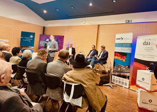 Ein Redner spricht vor Publikum bei einer Veranstaltung mit Panelisten und Bannern zu deutsch-atlantischen und deutsch-amerikanischen Beziehungen.