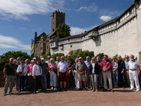 Eine Gruppe Erwachsener steht vor der Wartburg, einer historischen deutschen Festung mit Flagge auf dem Turm, unter blauem Himmel.