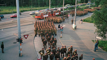 Militärparade auf der Treskowallee mit marschierenden Soldaten, einer roten Straßenbahn und Autos.