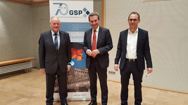 Drei Männer in Anzügen vor einem GSP-Banner, das das 70-jährige Bestehen der Gesellschaft für Sicherheitspolitik e.V. (1952-2022) zeigt.