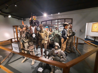 Museumsausstellung mit Militärmannequins in Uniformen aus verschiedenen Epochen, darunter ein Reiter und Fußsoldaten hinter einem Geländer.