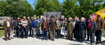 Gruppe von Männern, inkl. Soldat, vor Gedenkstein des 2. Stryker Cavalry Regiments mit Blumenkranz.