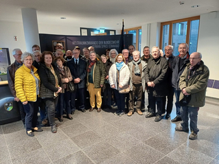 Eine große Gruppe älterer Erwachsener, Männer und Frauen, posiert lächelnd vor einem Banner des "Deutschen Weltraumkommandos".