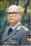 Porträt eines glatzköpfigen Mannes mit Brille in deutscher Bundeswehruniform, mit Namensschild 'FUCHS' und Flaggen-Patch.