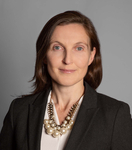 Professionelles Porträt einer Frau mit braunen Haaren und leichtem Lächeln, trägt einen dunklen Blazer und eine Perlenkette.