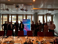 Gruppenfoto von diversen Fachleuten in einem modernen Büro, die hinter einem Konferenztisch mit einem 'NewSpace BDI Initiative'-Banner stehen.