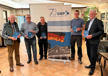 Fünf Männer halten blaue „Leitbild“-Broschüren vor einem GSP-Banner, das 70 Jahre Sicherheitspolitik feiert.