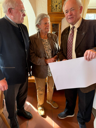Drei ältere Personen, zwei Männer und eine Frau, stehen in einem Raum. Der rechte Mann hält ein leeres Blatt Papier.