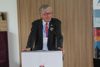 Dr. Hans-Peter Bartels, ein Mann im Anzug und Krawatte, spricht an einem Rednerpult mit Mikrofon bei einer Veranstaltung.