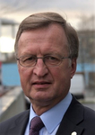 Porträt eines Mannes mittleren Alters mit Brille, hellbraunem Haar, Anzug, blauem Hemd und Krawatte.