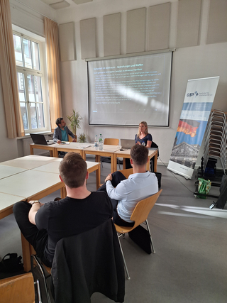 Eine Frau präsentiert zum Thema „Sicherheit im Weltraum“ vor einem Publikum in einem Hörsaal, mit GSP-Banner.