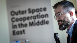 Ein bärtiger Mann mit Brille spricht in ein Mikrofon bei einer Konferenz über Weltraumkooperation im Nahen Osten.