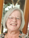 Kopfporträt einer lächelnden älteren Frau mit kurzen grauen Haaren und Brille.