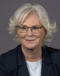 Lächelndes Porträt von Christine Lambrecht, einer Frau mit blonden Haaren und Brille, die einen dunklen Blazer trägt.
