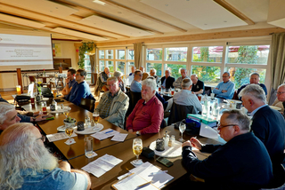 Ein GSP Fulda Treffen in Bronnzell mit Männern an Tischen, ein Bildschirm zeigt eine deutsche Präsentation über Europas Werte.