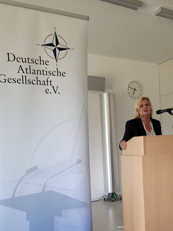 Frau spricht an Rednerpult vor einem Banner der 'Deutsche Atlantische Gesellschaft e.V.' mit NATO-Stern.