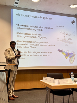 Ein Mann im Anzug präsentiert zum Thema 'Wie fliegen hypersonische Systeme?' von einer DLR-Folie mit Auftriebsdiagrammen.