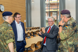 Vier Männer, zwei in Bundeswehr-Uniformen und zwei in Anzügen, führen ein angeregtes Gespräch in einem großen Raum.