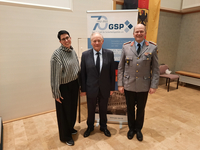 Drei Personen: Frau, Mann im Anzug, Mann in Militäruniform, vor GSP-70-Jahre-Banner und deutscher Flagge.
