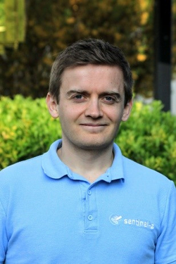 Porträt eines lächelnden Mannes mit braunen Haaren in einem hellblauen Poloshirt mit einem 'sentinel-2'-Logo.