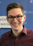 Lächelnder junger Mann mit Brille und weinrotem Hemd vor blauem Hintergrund mit Konrad-Adenauer-Stiftung-Logo.