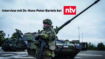 Soldat in Tarnuniform mit Gewehr vor Militärfahrzeugen. Text: "Interview mit Dr. Hans-Peter-Bartels bei ntv" und NTV-Logo.