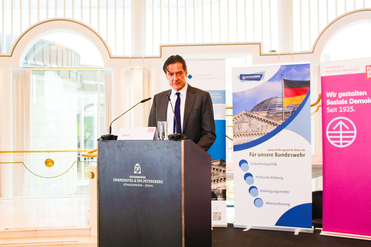 Ein Mann im Anzug spricht an einem Podium mit dem Namen 'Sauer'. Im Hintergrund stehen Banner zur Sicherheitspolitik und Sozialen Demokratie.
