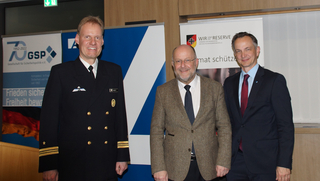 Drei Männer, darunter ein Marineoffizier, posieren vor Bannern der GSP und des Reservistenverbandes.