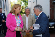Drei Personen unterhalten sich: eine Frau in pinkem Blazer, ein Mann in blauem Anzug und ein lächelnder Mann in hellem Sakko.