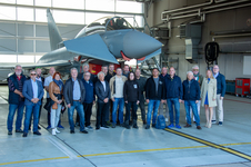 Eine Gruppe Erwachsener posiert vor einem Eurofighter Typhoon Militärjet in einem hellen Flugzeughangar.